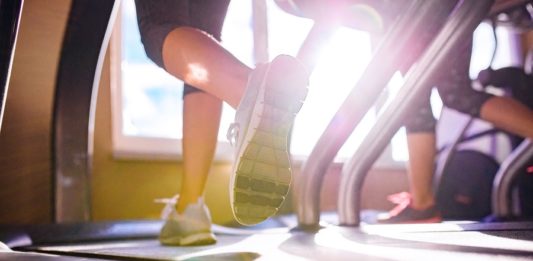 Best Running Shoes for Treadmill in 2020 Close up of legs of two women running on treadmills in a gym, sunny day with top rated shoes